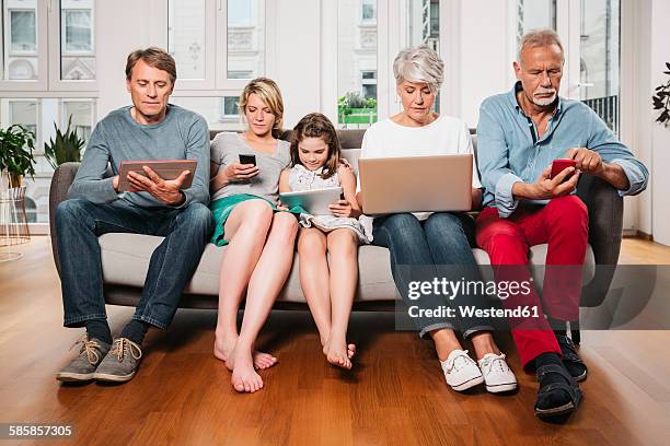 group picture of three generations family sitting on one couch using different digital devices - family formal portrait stock pictures, royalty-free photos & images