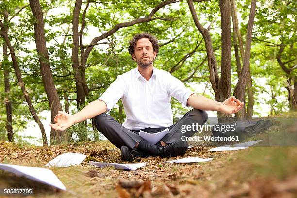 germany, businessman in forest surrounded by papers practising yoga - businessman meditating stock pictures, royalty-free photos & images