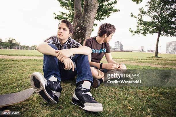 germany, berlin, two teenage boys in bad mood sitting under a tree - friends argue fotografías e imágenes de stock