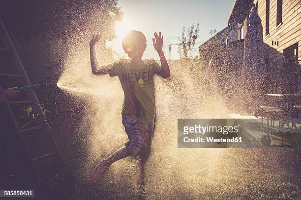 boy and girl having fun with splashing water in the garden - wet hose ストックフォトと画像