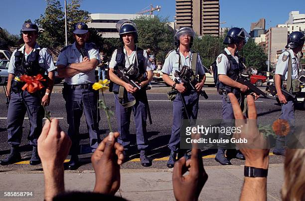 White Johannesburg riot police threaten anti-apartheid student protesters at the University of Witwatersrand who are holding flowers and flashing...