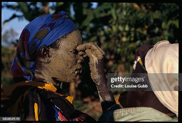 Young Sabiny girl prepares for a circumcision ceremony by having her face painted with mud by an elderly "caregiver." While a traditional rite of...