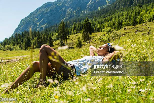 austria, tyrol, tannheim valley, young woman relaxing in meadow - état fédéré du tyrol photos et images de collection