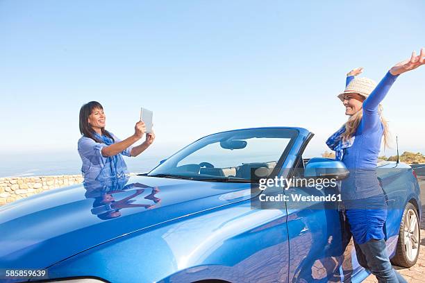 south africa, two happy women at a convertible taking pictures with a digital tablet - toyota south africa motors stock pictures, royalty-free photos & images