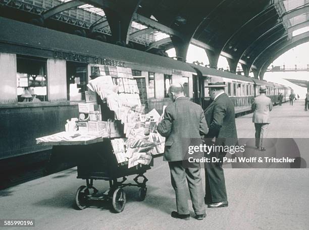 Men standing in front of a stand for newspapers in a station