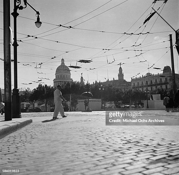 Man walks across a street underneath the electric cables for cable cars , showing the Capital building in the distance in Havana, Cuba.