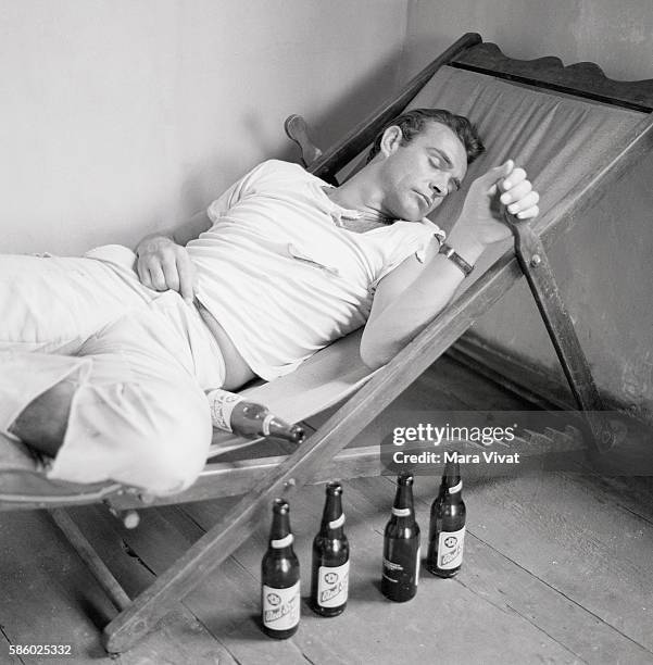 Actor Sean Connery sleeps on a lounge chair beside a row of empty Red Stripe beer bottles, possibly in character for a movie role. Connery played...