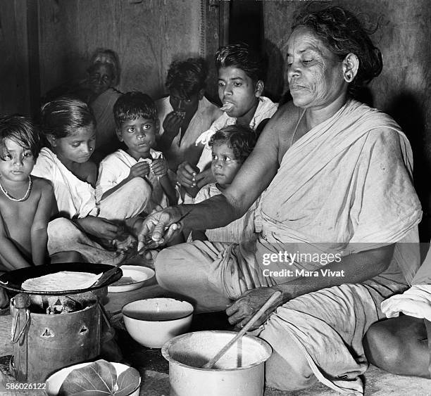 An Untouchable woman cooks dinner in hut while children look on. Madras, India.