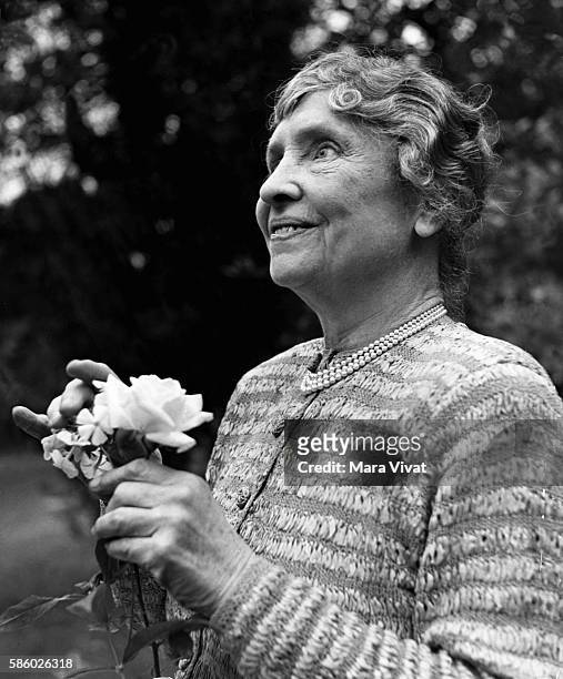 Teacher and author Helen Keller holds a rose in a garden. Keller achieved wide recognition by overcoming blindness and deafness to become a notable...