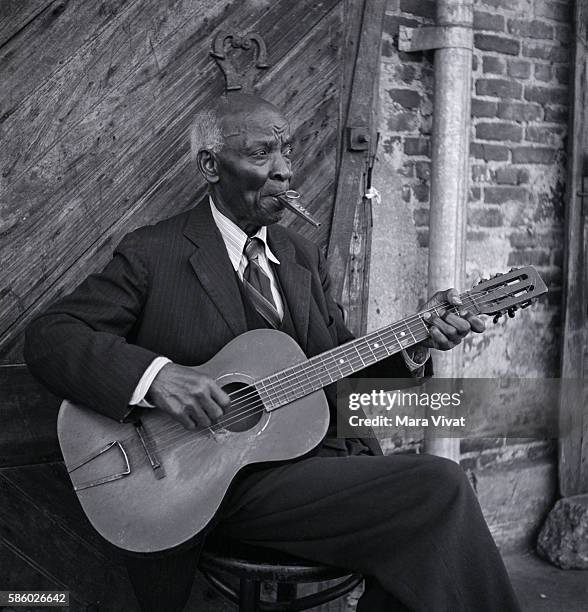 An elderly musician plays the guitar and kazoo simultaneously.