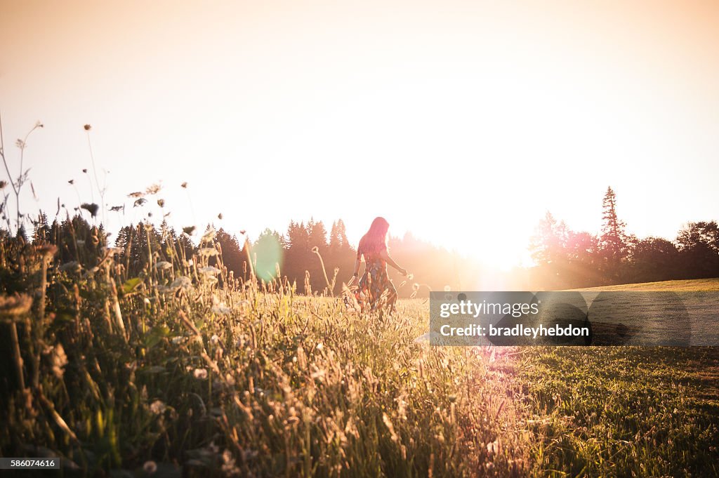 Woman walking through meadow at sunset