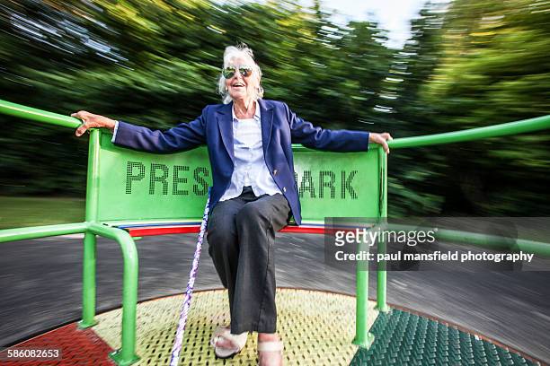 senior lady enjoying playground ride - paul mansfield photography stock-fotos und bilder