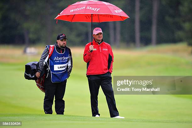 Paul Lawrie of Scotland shelters under an umbrella on the green at hole 1 on day two of the Aberdeen Asset Management Paul Lawrie Matchplay at...