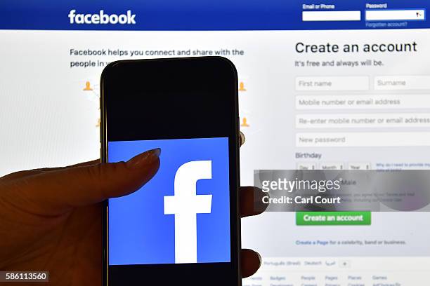 Person holds an iPhone displaying the Facebook app logo in front of a computer screen showing the facebook login page on August 3, 2016 in London,...