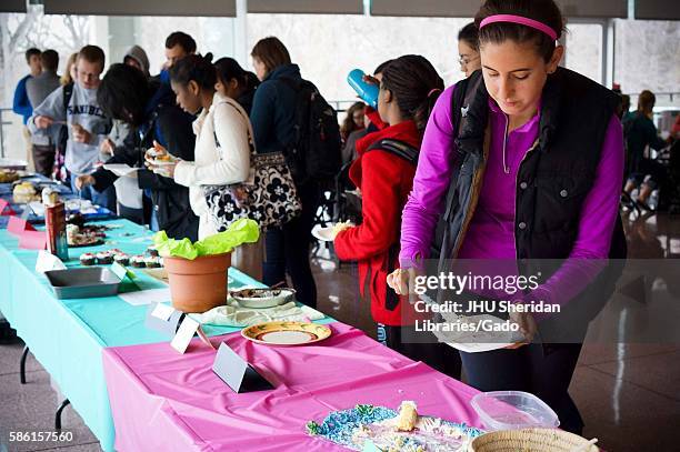 College students crowd around the long table to try various types of cake at the Edible Book Festival, April, 2014. Courtesy Eric Chen. .