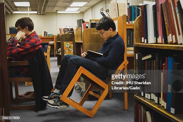Surrounded by books, college students study, one of them leaning his chair back, in the Milton S. Eisenhower Library on the Homewood campus of the...