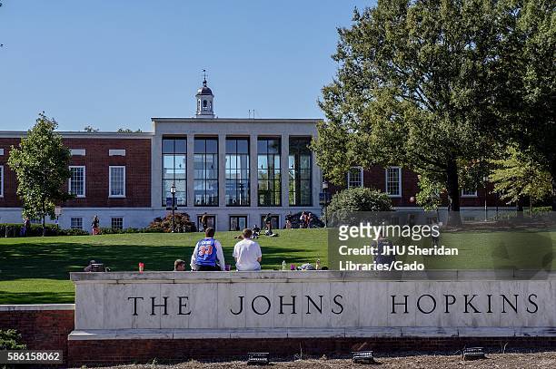 View from Charles street of the grassy "Beach" and Milton S Eisenhower Library of the Johns Hopkins University; three male students, their backs...