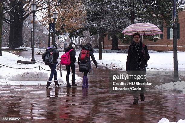 Male graduate student holding an umbrella walks towards the camera as three female undergraduate students in warm clothes and snow boots walk behind...