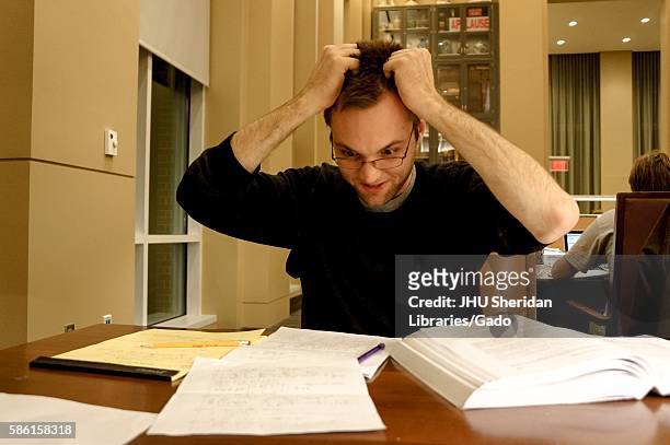 Flustered college student grabs his hair as he looks at his notes in the Reading Room of the Brody Learning Commons, a study space and library on the...