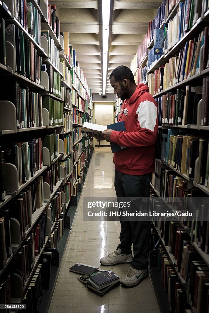 A student stands and reads a book among the stacks in the Milton S ...