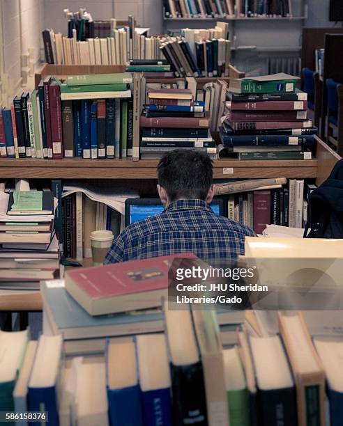 Graduate student sits at his work station on his laptop, surrounded by piles of books, in the Milton S. Eisenhower Library on the Homewood campus of...
