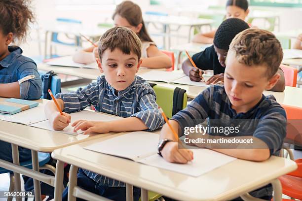 elementary students taking a test in classroom. - dishonesty stock pictures, royalty-free photos & images