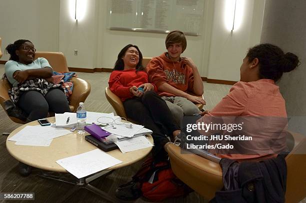 Four students sitting in three chairs in the Brody Learning Commons at Johns Hopkins University, surrounded by study materials, laughing facial...