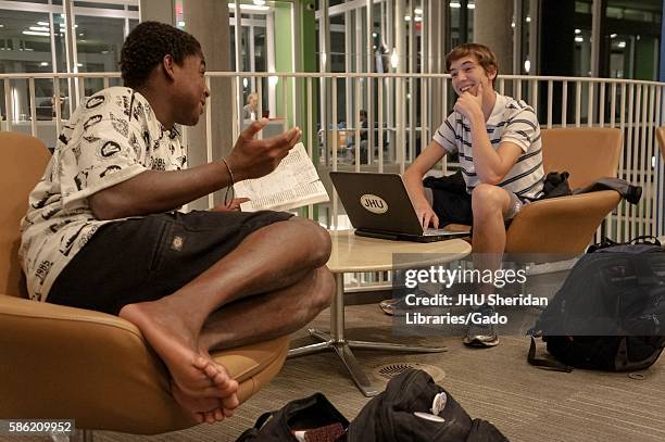 Two male students sitting on chairs of the first floor, Q level, of the Brody Learning Commons at Johns Hopkins University, surrounded by study...
