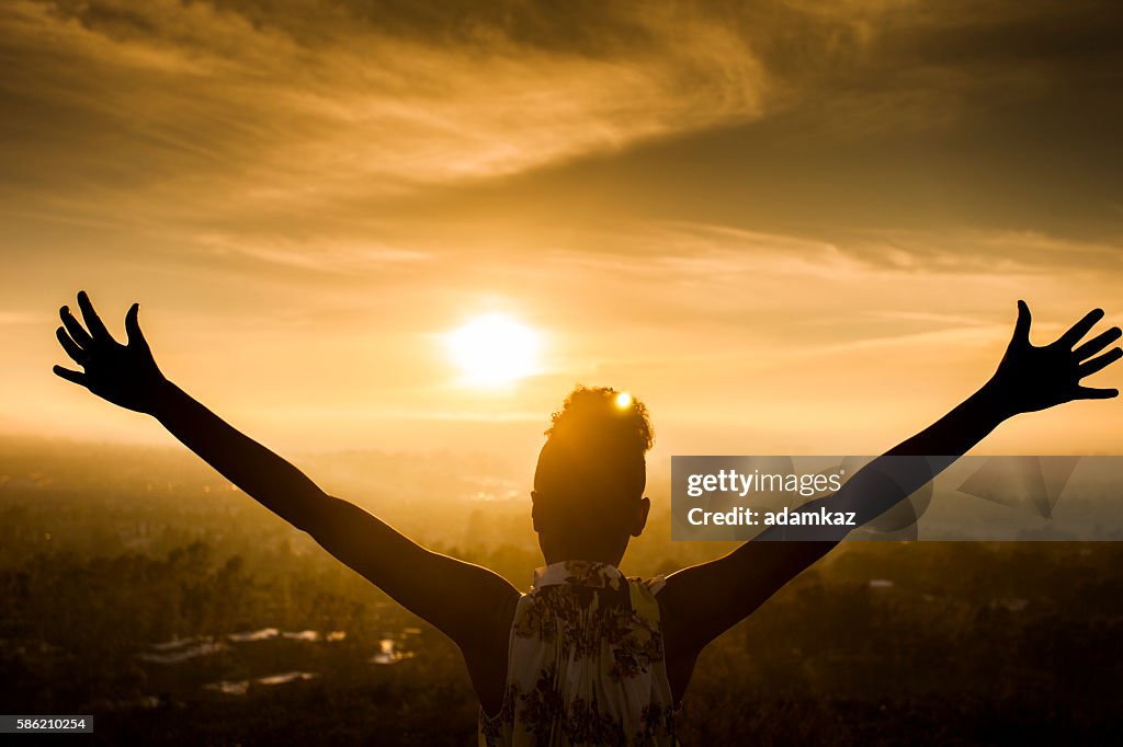 Donna afroamericana che alza le braccia al tramonto