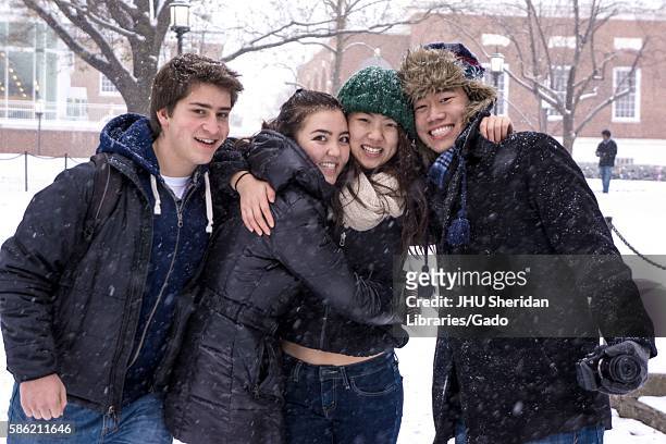 Four freshman college students at the Johns Hopkins University gather together and smile in front of the Milton S. Eisenhower Library as snow falls...