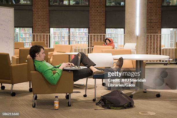Student with his feet up studies on his laptop while his peer naps nearby, on the ground floor of the Brody Learning Commons, an...