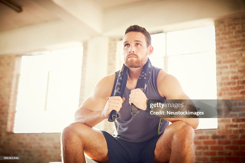 Tired young man with towel around neck in gym