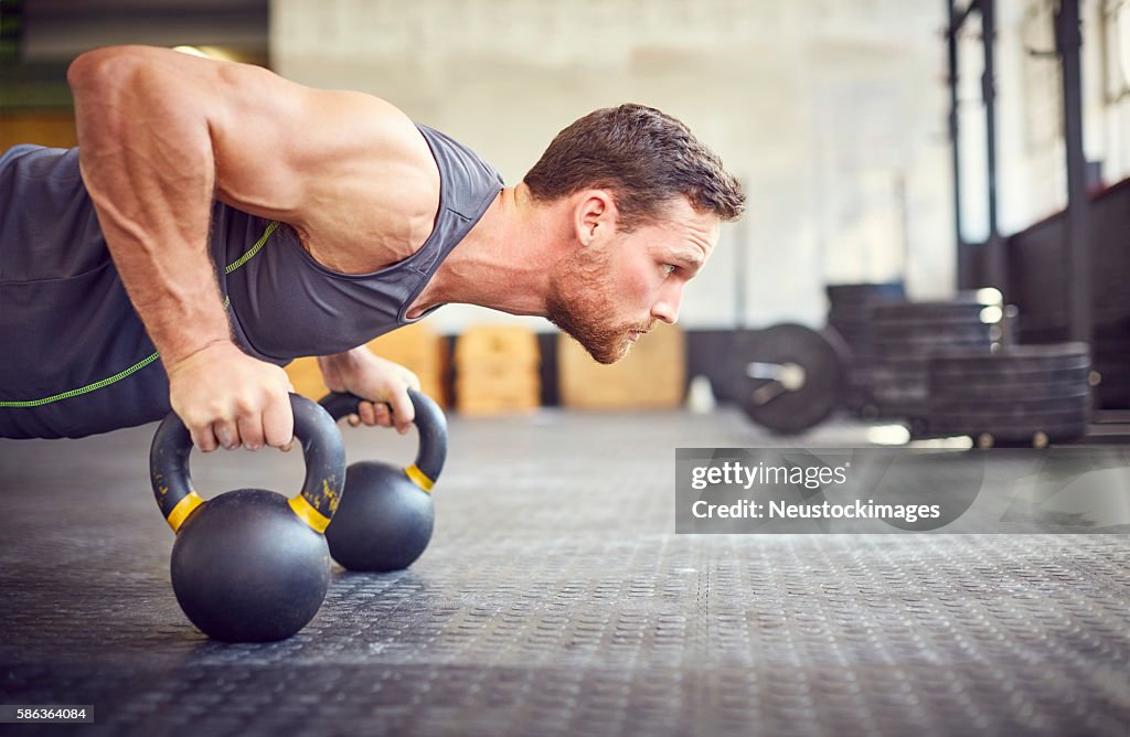 Determined athlete doing push-ups on kettlebells in gym