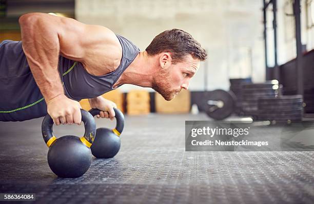 determined athlete doing push-ups on kettlebells in gym - toughness man stock pictures, royalty-free photos & images