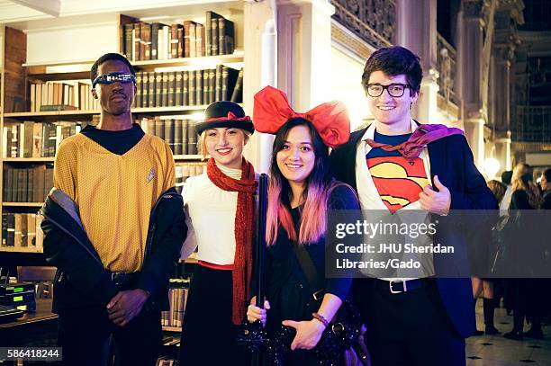 Four college students are in costume and are posing, the boy on the far right is dressed as Superman and the girl next to him is wearing a large red...