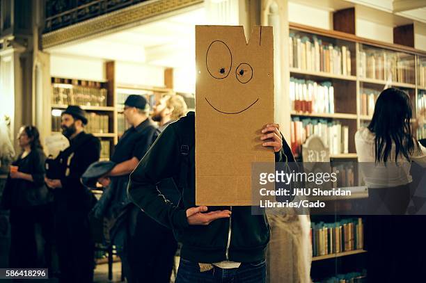 Student shown holding up the Plank from the television show "Ed, Ed, n Eddy"; party-goers shown in the background with the library stacks, Halloween...