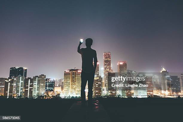 businesswoman on rooftop holding cell phone - linghe zhao stock pictures, royalty-free photos & images