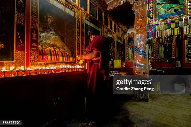 Lama monk lights butter lamps in front of Buddha statue. Kumbum Monastery is one of the two most important Tibetan Buddhist monasteries outside...
