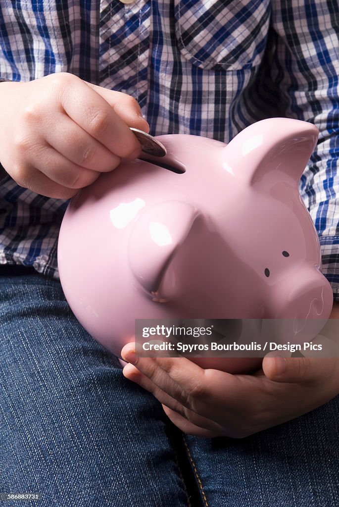 Young Boy Depositing Coins Into A Piggy Bank