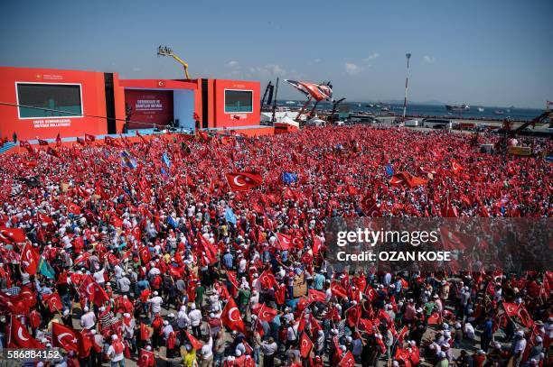 Demonstrators wave Turkish national flags as they stand in front of giant screens on August 7, 2016 in Istanbul during a rally against failed...