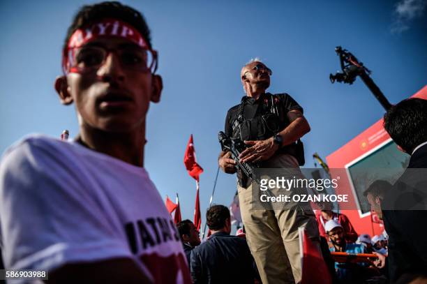 Turkish special force police officer stands guard as people shout slogans and wawe Turkish national flags on August 7, 2016 in Istanbul during a...