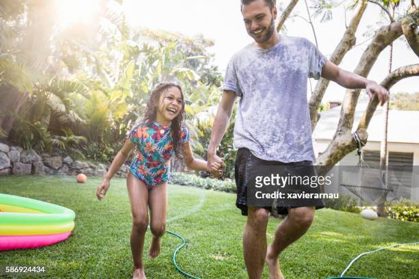 aborigine-vater und tochter mit spaß im garten - family playing in backyard pool stock-fotos und bilder