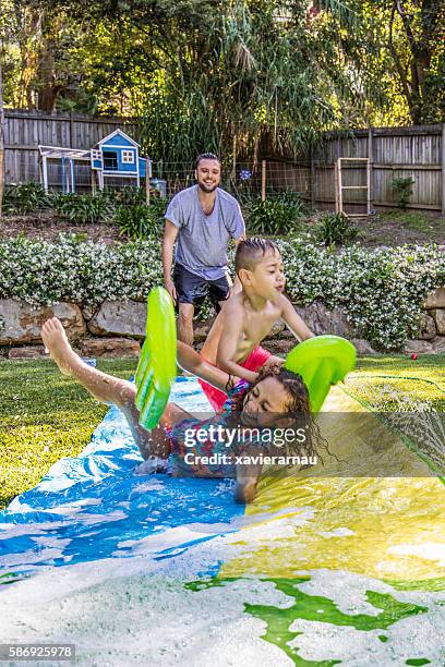 aboriginal children on slip 'n slide in the garden - backyard water slide stock pictures, royalty-free photos & images