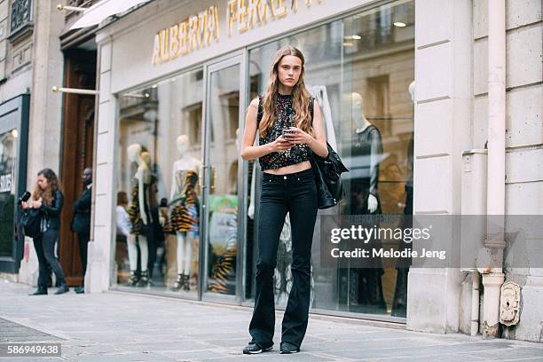 Dutch model Tia Brandsma holds her phone and wears a black floral sleeveless top and black flared jeans after the Alberta Ferretti show on Day 1 of...