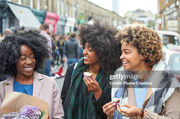 friends laughing and eating cupcakes at flower market. - black female friends stockfoto's en -beelden