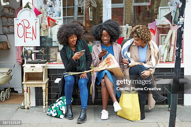 group of friends using their mobile phones outside a shop. - african lady sitting and looking at her smartphone stock-fotos und bilder