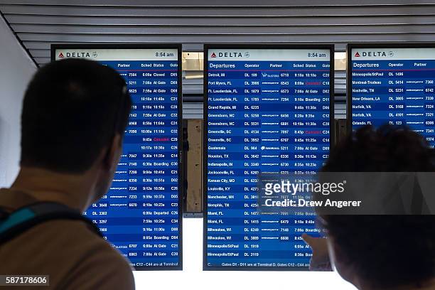 Travelers check the Delta departures board at LaGuardia Airport , August 8, 2016 in the Queens borough of New York City. Delta flights around the...