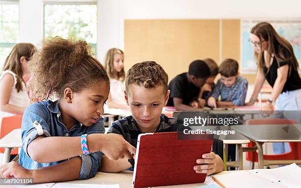school kids in class using a digital tablet - schoollokaal stockfoto's en -beelden