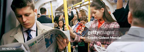 Commuters on a crowded carriage in the London underground seem to withdraw into their own private space as they read and listen to music.