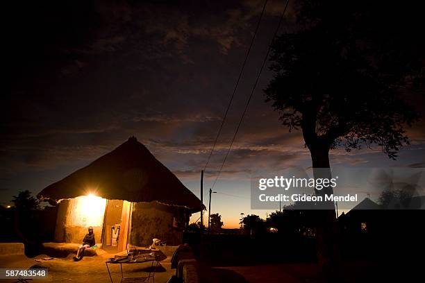 Traditional African sunset scene in the Makuleke village but an electric light provides illumination as night falls showing some of the benefits of...